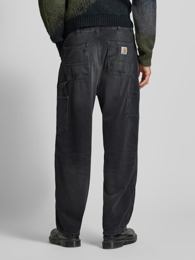Männermodel trägt Wide Fit Jeans Logo-Patch Modell 'Grind' von Carhartt Work In Progress in Schwarz mit 5-Pocket-Design aus reiner Baumwolle, Ganzkörperansicht Rückansicht.