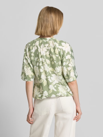 Vrouwenmodel draagt Relaxed Fit Blusenshirt uit viscosemix van s.Oliver RED LABEL met all-over bloemenmotief, kreuklook, groene en witte tinten, korte raglanmouwen, elastische rompzoom, detailopname rugaanzicht.