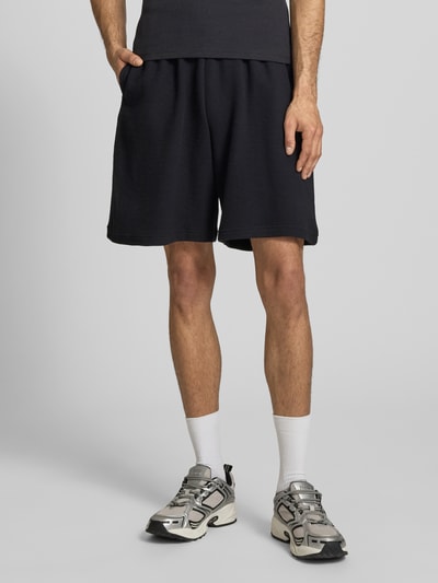 Männermodel trägt Regular Fit Shorts mit elastischem Bund von KARL KANI, Strukturmuster, Reine Baumwolle, Nahaufnahme Beine, Vorderansicht.