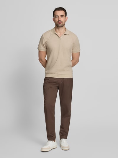 Męski model nosi Comfort Fit Poloshirt mit V-Ausschnitt von Lindbergh z bawełny, fakturowany wzór, detal z logo, długość tyłu 68 cm w rozmiarze M, widok całej sylwetki z przodu.