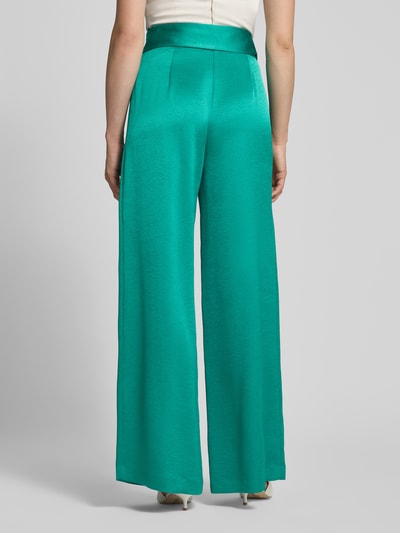 Frauenmodel trägt Relaxed Fit Anzughose aus Satin von Marc Cain in Türkis mit Crinkle-Optik und breitem Stoffgürtel, Ganzkörperansicht Rückansicht.
