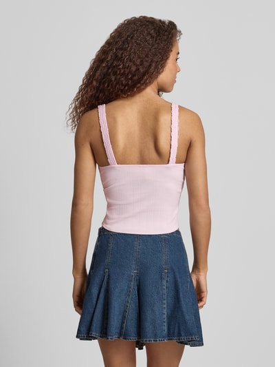 Frauenmodel trägt Slim Fit Top mit Spitzenbesatz von Guess Jeans in Rosa mit Zierschleife, elastischer Baumwoll-Mix mit Modal-Anteil, Ärmelloses-Design, V-Ausschnitt, Rückenlänge bei Größe S: 26 cm, Jeans-Minirockdje, Ganzkörperansicht Rückansicht.