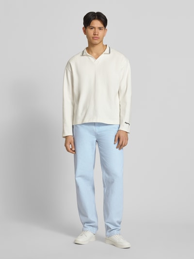 Männermodel trägt Loose Fit Jeans mit Kontrastnähten von KARL KANI in Hellblau, strukturierte Oberfläche, 5-Pocket-Design, Ganzkörperansicht von vorne.