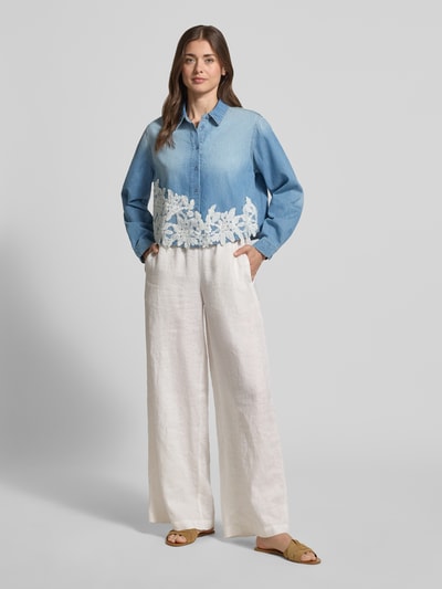 Frauenmodel trägt Regular Fit Hemdbluse in Denim-Optik mit Spitzenbesatz von More & More, Reine Baumwolle, Langärmelig, Hemdblusenkragen, durchgehende Knopfleiste, Rückenlänge 50 cm, Ärmellänge 58 cm, sanft blaue und weiße Farbtöne, glatte Struktur, floraler Spitzeneinsatz, Ganzkörperansicht von vorne.