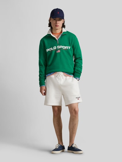 Männermodel trägt Relaxed Fit Troyer aus Baumwoll-Mix von Polo Ralph Lauren in Grün mit Label Print, kurzem Reißverschluss, Ganzkörperansicht von vorne.