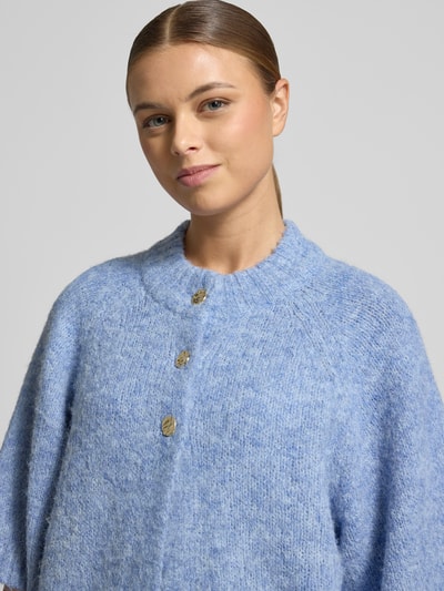 Frauenmodel trägt Strickjacke mit Knopfleiste Modell 'Benutta' von Neo Noir in Hellblau, gerippte Abschlüsse, Nahaufnahme Oberkörper.