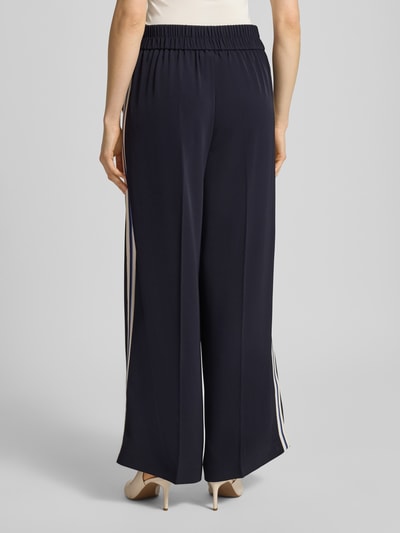 Frauenmodel trägt Stoffhose mit elastischem Bund von Comma, dunkelblau, ausgestellter Schnitt, Ziernähte, Material-Mix mit Stretch-Anteil, Ganzkörperansicht Rückansicht.