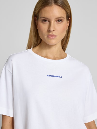 Frauenmodel trägt Oversized T-Shirt aus reiner Baumwolle Modell 'GIANNAA CHAANGE' von Armedangels, weiß, blauer Label Print, Feinripp, Nahaufnahme Oberkörper.