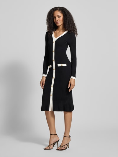 Vrouwenmodel draagt Slim Fit Tricotjurk uit viscosemix Model 'Laurel' van Guess in zwart-wit met knoopsluiting, zakken, V-hals, lang mouw, ruglengte 110 cm, borstwijdte 33 cm, mouwlengte 63 cm, effen structuur, Ganzkörperansicht van voren.