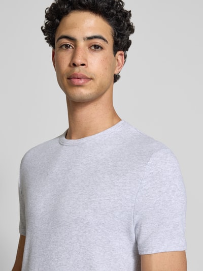 Męski model nosi T-Shirt in Feinripp mit Rundhalsausschnitt od REVIEW, bawełniana mieszanka z domieszką stretchu, krój slim fit, faktura prążkowana, jasnoszary kolor, detal z logo, długość pleców w rozmiarze M: 64 cm, zbliżenie na górną część ciała z przodu.
