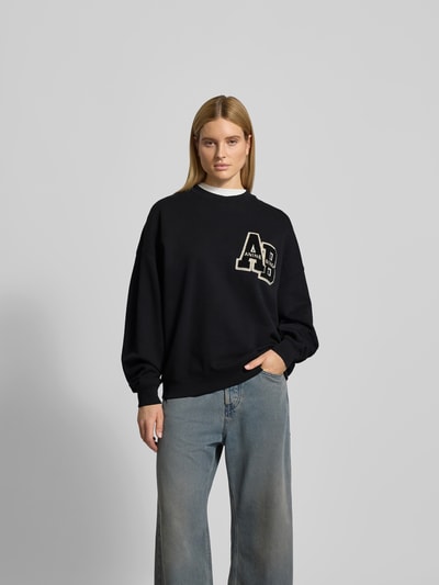 Frauenmodel trägt Oversized Sweatshirt mit Logo-Detail von Anine Bing in Schwarz, Reine Baumwolle, Oversized-Fit, Rundhalsausschnitt, elastische Abschlüsse, Rückenlänge bei Größe S 64 cm, Ganzkörperansicht von vorne.