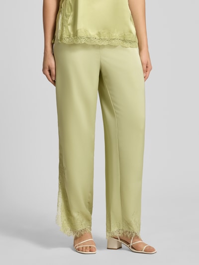Frauenmodel trägt Flared Fit Stoffhose mit Spitzenbesatz von Gina Tricot in gelbgrüner Satin-Optik, elastischer Bund mit Tunnelzug, Damen, Nahaufnahme Unterkörper, Bundweite 40 cm, Innenbeinlänge 79 cm, Größe S, Ganzkörperansicht von vorne.