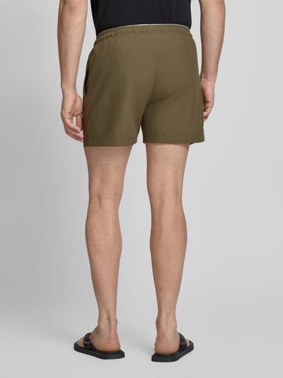 Männermodel trägt Relaxed Fit Badeshorts mit Logo-Stitching von Emporio Armani in Oliv, Elastischer Bund mit Tunnelzug, Ganzkörperansicht Rückansicht.