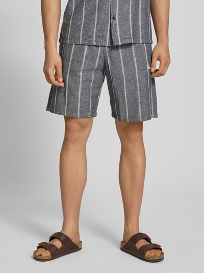 Männermodel trägt Leinenshorts mit Logo-Stitching von REVIEW, grau mit weißen Streifen, seitliche Taschen, Nahaufnahme Oberschenkel.