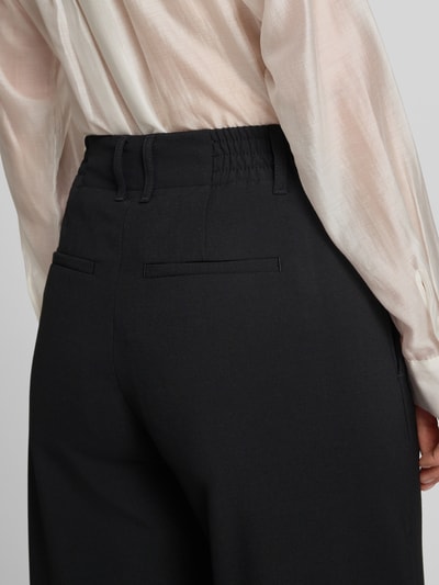 Frauenmodel trägt schwarze Wide-Fit Damen Stoffhose mit Viskose-Anteil, Modell 'Dutiful' von Drykorn, Gesäßtaschen, Elastischer-Material-Mix, Haken-Reißverschluss, Detailaufnahme Rückansicht.