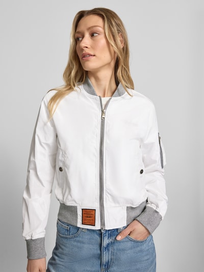 Frauenmodel trägt Bomberjacke mit Label-Patch und Reißverschlusstasche am Ärmel von Original Bombers in Weiß mit grauen elastischen Abschlüssen, silbernem Reißverschluss, seitlichen Eingrifftaschen und Logo-Stitching, Lockerer-Schnitt, Stehkragen, Ganzkörperansicht von vorne.