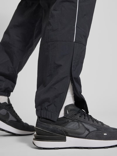 Männermodel trägt Trainingshose mit Logo und elastischem Bund von Nike in Schwarz, Relaxed-Fit, elastische Beinabschlüsse, Nahaufnahme Bein, Innenbeinlänge bei Größe M: 76 cm.