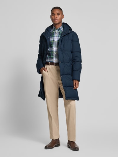 Männermodel trägt Steppmantel mit Kapuze und Eingrifftaschen von Christian Berg Men in Dunkelblau, Regular Fit, Ganzkörperansicht von vorne.