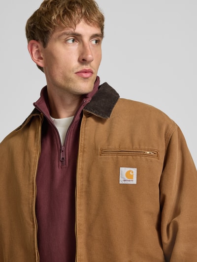 Männermodel trägt Blouson mit Brusttasche Modell 'DETROIT' von Carhartt Work In Progress in Braun, Nahaufnahme Oberkörper. Regular Fit, Kentkragen in Cord-Optik, Reißverschluss, Label-Patch, Brusttasche mit Reißverschluss, seitliche Eingrifftaschen, Größe M: Rückenlänge 69 cm, Schulterbreite 48 cm, Brustweite 60 cm, Ärmellänge 63 cm.
