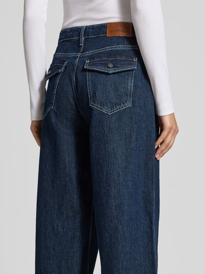Frauenmodel trägt Wide Fit Jeans mit Logo-Patch von GUESS in dunklem Blau, 5-Pocket-Design, Ganzkörperansicht Rückansicht.