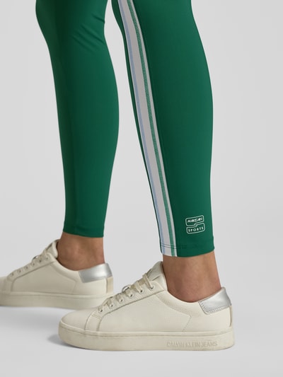Männermodel trägt Slim Fit Leggins mit elastischem Bund von Marc Cain, elastyczna mieszanka materiałów, krój slim fit, elastyczny pas, ozdobne obszycie, szerokość w rozmiarze 36: 34 cm, długość wewnętrzna nogawki w rozmiarze 36: 76 cm, zielony kolor, gładka tekstura, prosty kształt, detailaufnahme nogawki