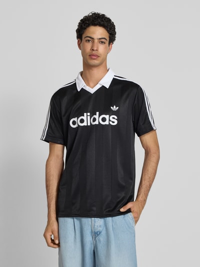 Männermodel trägt Regular Fit Trikot-Shirt mit Polokragen von adidas Originals, Optik: Unifarben, Label-Schriftzug, Kontraststreifen, V-Ausschnitt, Passform: Regular-Fit, Kragenform: Polokragen, Ärmelform: Kurzarm, Ganzkörperansicht von vorne.