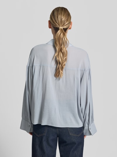 Frauenmodel trägt Relaxed Fit Bluse Modell 'SELENI' von Drykorn aus Baumwoll-Viskose-Mix in Hellblau, Rückenansicht, Ganzkörperansicht Rückansicht.