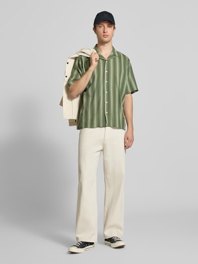 Männermodel trägt Regular Fit Freizeithemd mit Reverskragen Modell 'HOWIE' von Redefined Rebel in grünem Allover-Look aus Reiner Baumwolle, Knopfleiste, kombiniert mit heller Hose, Ganzkörperansicht von vorne. Rückenlänge bei Größe M: 60 cm, Schulterbreite: 60 cm, Ärmellänge: 30 cm, Label-Detail.