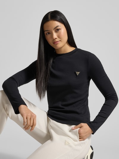 Frauenmodel trägt Longsleeve mit Label-Detail Modell 'SONIA' von Guess aus reiner Baumwolle, Regular Fit, schwarzer Stoff, Nahaufnahme Oberkörper.