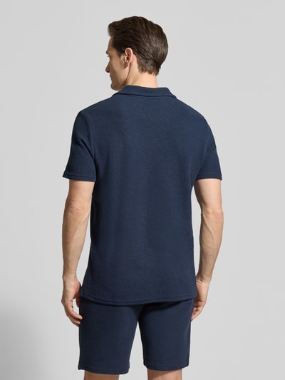 Męski model nosi Regular Fit Poloshirt aus Baumwoll-Mix von MCNEAL, mieszanka bawełny i elastanu, pika, wykładany kołnierz, dekolt w serek, krótki rękaw, długość tyłu w rozmiarze M: 69 cm, ciemnoniebieski, jednolita faktura, krój regular fit, widok całej sylwetki z tyłu.