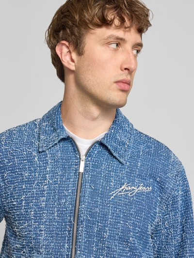 Männermodel trägt Regular Fit Jacke in denimlook met structuurpatroon van KARL KANI, puur katoen, gestikt logo, platte kraag, steekzakken, ritssluiting, herenjack, kleur blauw-wit, textuur grof, nahaufnahme oberkörper. Ruglengte maat M: 64 cm, schouderbreedte: 50 cm, borstwijdte: 57 cm, mouwlengte: 69 cm.