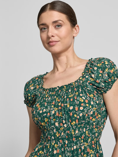Modelka kobieca nosi Midikleid aus Viskose mit Smok-Details od Apricot, zielony materiał z kwiatowym wzorem, krój dopasowany, okrągły dekolt z falbaną, rękawy z falbaną, Szerokość w rozmiarze S: 40 cm, długość tyłu: 105 cm, zbliżenie na górną część ciała.