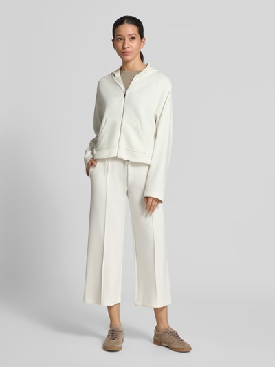 Modelka kobieca ma na sobie Regular Fit Sweatjacke mit Kapuze Modell 'Marcella' od Christian Berg Woman z elastycznej mieszanki materiałów z domieszką modalu, z kapturem, podzieloną kieszenią kangurka i pasem z tunelem, całość w jasnym odcieniu, gładka tekstura, krój regular fit, widok całej sylwetki z przodu.