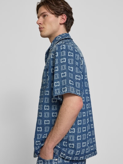 Männermodel trägt Relaxed Fit Freizeithemd in Denim-Optik mit Allover-Logo-Print von COLUCCI aus reiner Baumwolle, Nahaufnahme Oberkörper.