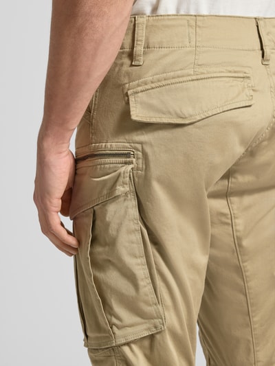 Mężczyzna nosi Regular Tapered Fit Spodnie cargo z kieszenią zapinaną na zamek od G-Star RAW, mieszanka bawełny i elastanu, model Rovic, 5 kieszeni, szlufki, kolor beżowy, widok szczegółowy na tylne i boczne kieszenie, detal.