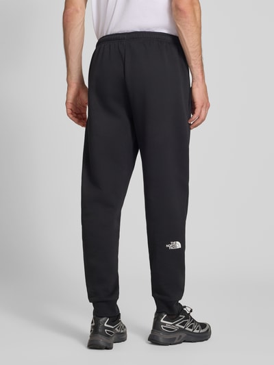 Mężczyzna nosi Regular Fit Sweatpants aus Escorial-Mix od The North Face, czarne, wpuszczane kieszenie, nadruk z logo, mieszanka wełny escorial i bawełny, krój regular fit, elastyczny pas z tunelem, długość wewnętrzna nogawki w rozmiarze M: 75 cm, widok całej sylwetki od tyłu.
