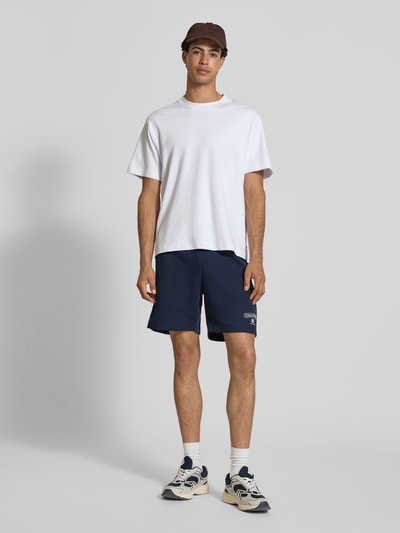 Männermodel trägt dunkelblaue Sweatshorts mit Logo und elastischem Bund von CHAMPION aus Baumwoll-Mix, Regular Fit, Ganzkörperansicht von vorne.