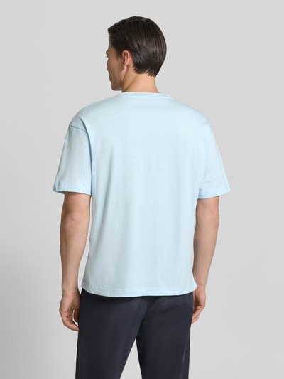 Męski model nosi Regular Fit T-Shirt mit Label-Schriftzug aus reiner Baumwolle od Tommy Hilfiger, jasnoniebieski, krój regular fit, unikatowa faktura bawełny, prosty fason, jednolity kolor, widok całej sylwetki z tyłu.