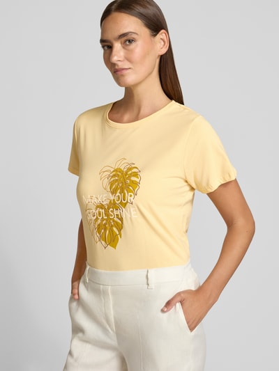 Kobiece modelka nosi T-shirt mit Statement- und Motiv-Print Modell 'RINA' od Soyaconcept z czystej bawełny, krój regular fit, okrągły dekolt, długość tyłu w rozmiarze S: 60 cm, jasny żółty, nadruk z motywem roślinnym, widok z przodu, zbliżenie na górną część ciała.