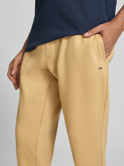 Männermodel trägt Slim Fit Sweathose aus Baumwoll-Mix von Tommy Jeans in Beige mit dezenter Logo-Stickerei, Nahaufnahme Oberkörper