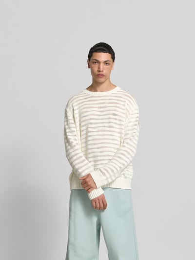 Männermodel trägt Relaxed Fit Pullover in Strick-Optik von MM6 Maison Margiela aus reiner Baumwolle, Rundhalsausschnitt, elastische Abschlüsse, Rückenlänge bei Größe M 67 cm, helle Farben, dezente Streifen, weiche Textur, Ganzkörperansicht von vorne.