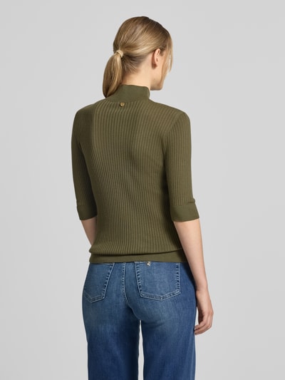 Frauenmodel trägt Slim Fit Longsleeve aus reiner Lanawolle Modell 'Maglia Costine' von Liu Jo White in Olivgrün, Rippenstruktur, Stehkragen, Halbarm, semitransparentes Design, Rückenlänge 58 cm, Ärmellänge 34 cm, Ganzkörperansicht Rückansicht.