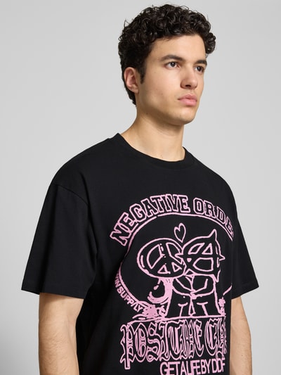 Männermodel trägt Herren T-Shirt mit Motiv-Print Modell 'POSITIVE CHAOS' von Edwin, Schwarz mit Rosa, Reine Baumwolle, Relaxed-Fit, Nahaufnahme Oberkörper.