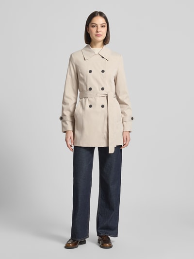 Kobiece model nosi Regular Fit Trenchcoat mit Taillengürtel zum Binden Modell 'CHALSEA OLIVIA' od Vero Moda, efekt: jednolity kolor, krój regular fit, wykładany kołnierz, listwa guzikowa 2-rzędowa, szwy, długi rękaw, zakończenie rękawów z patką, wpuszczane kieszenie, wykończenie materiału: splot twill, widok całej sylwetki z przodu.