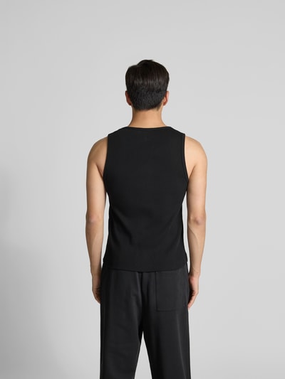 Männermodel trägt schwarzes Top aus reiner Baumwolle von MAISON KITSUNÉ, eng anliegend, Ripp-Optik, ärmellos, Rückansicht, Ganzkörperansicht.