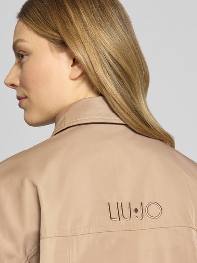 Frauenmodel trägt Jacke mit Kimonoärmeln und Pattentaschen von LIU JO SPORT, glatter beige Material-Mix, Nahaufnahme Rückansicht.