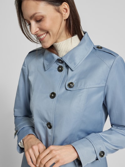 Frauenmodel trägt Trenchcoat mit Ärmelriegeln von Fuchs Schmitt in Hellblau, glatte Textur, sichtbare Knopfleiste, Nahaufnahme Oberkörper. Regular Fit, Umlegekragen, Eingrifftaschen.