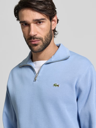 Männermodel trägt Regular Fit Troyer aus reiner Baumwolle von Lacoste in Hellblau mit Logo-Patch, Nahaufnahme Oberkörper.
