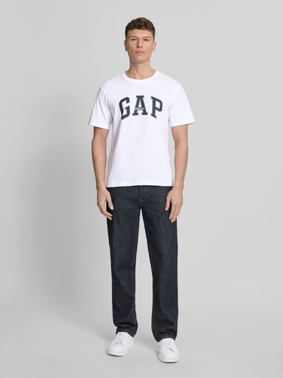 Männermodel trägt T-Shirt mit Logo und Rundhalsausschnitt von GAP, Herren T-Shirt aus Reine Baumwolle, Regular-Fit, weiße Farbe, Ganzkörperansicht von vorne. Rückenlänge bei Größe M: 66 cm.