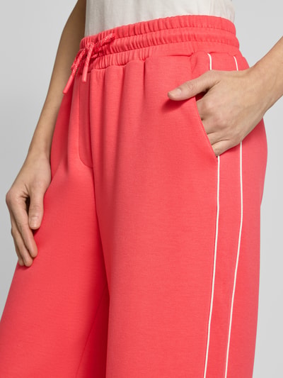 Frauenmodel trägt Wide Fit Sweatpants mit elastischem Bund Modell 'KATE NEO' von ICHI in Koralle mit weißen Zierstreifen, Nahaufnahme Oberkörper, Material-Mix mit Viskose-Anteil, elastischer Bund und Tunnelzug.